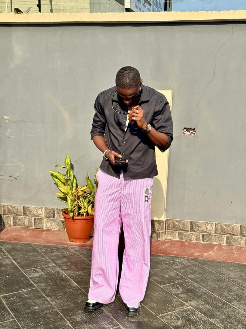 Dark overshirt worn with pink wide-leg trousers against a pink wall